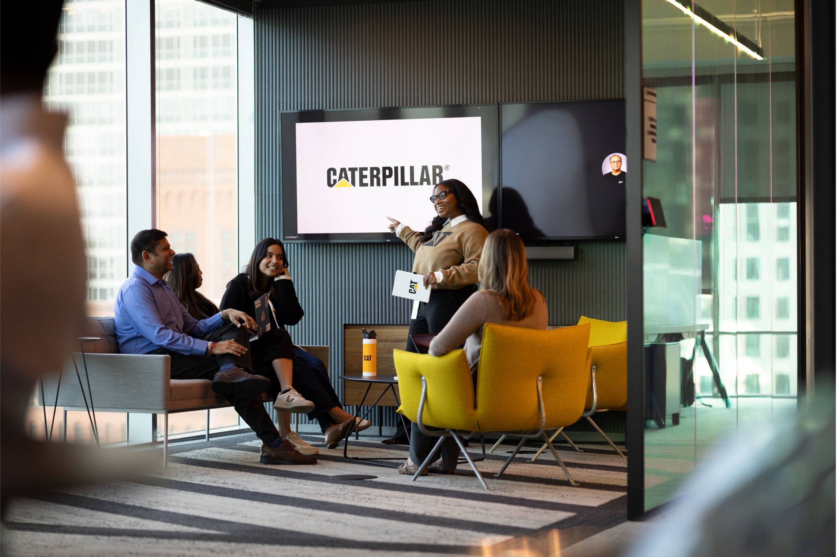 a group of people sitting in chairs and a person pointing at a screen