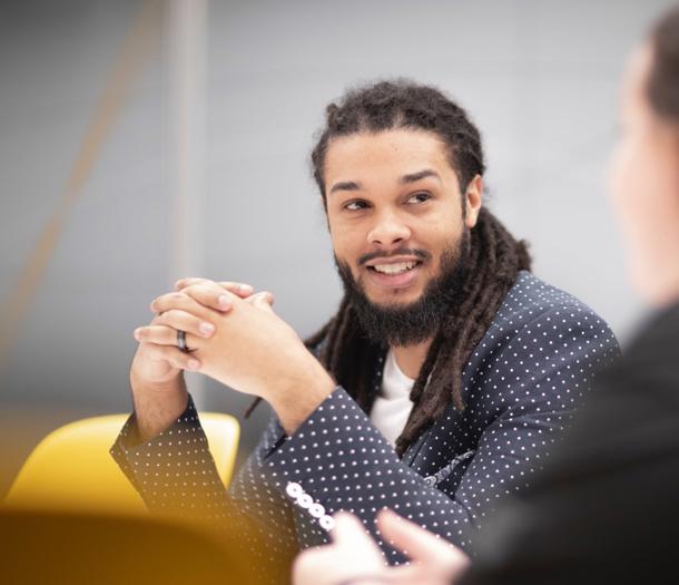 une personne avec des dreadlocks assise dans une pièce avec un groupe de personnes