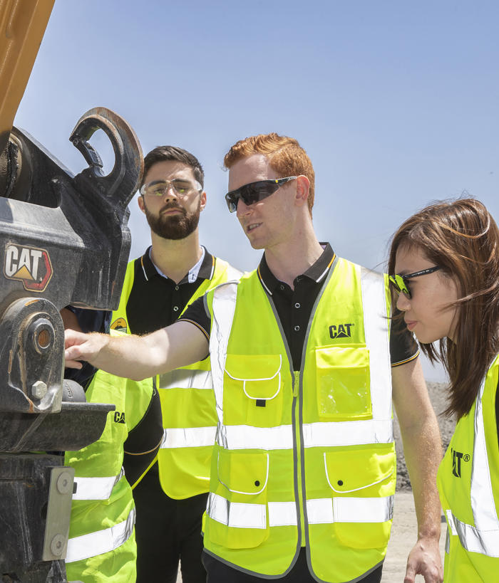 a group of people in safety vests looking at a machine